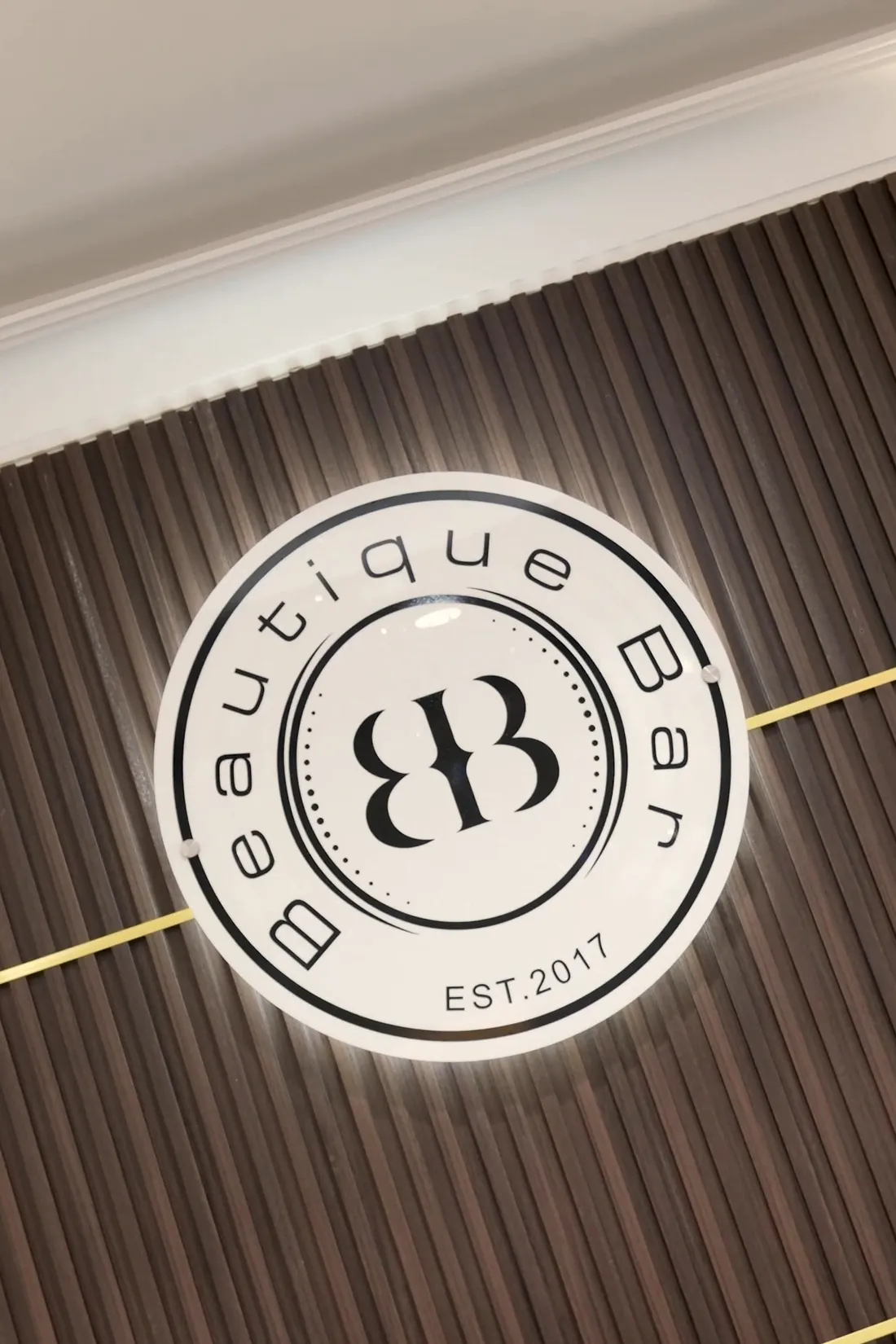The Beautique Bar logo lit on the wood-slat wall